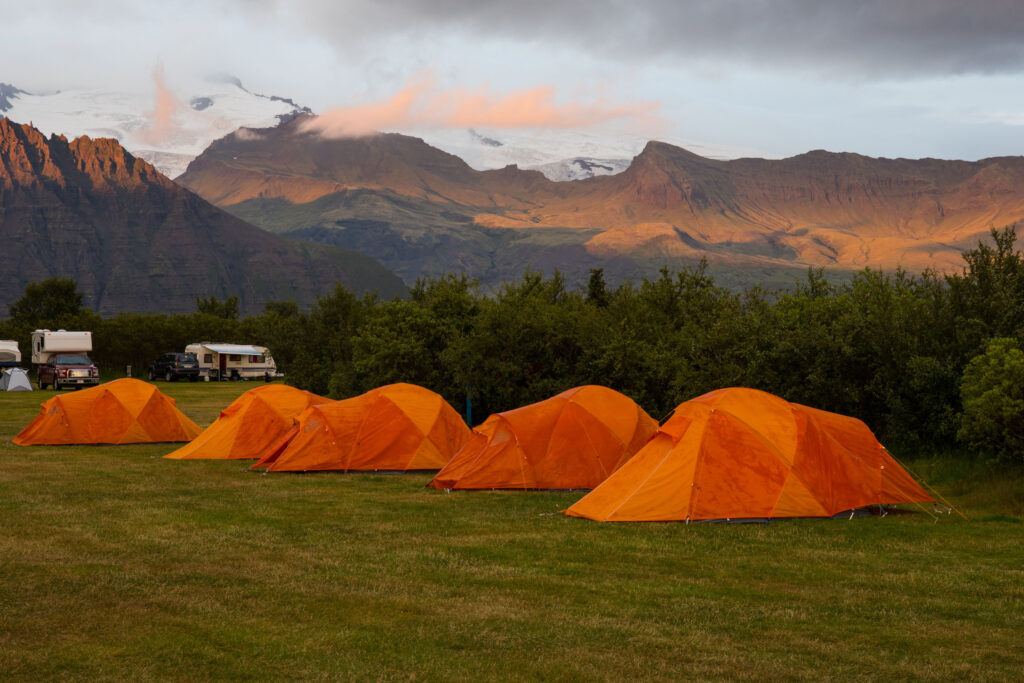 Orange tents in a campground in front of gorgeous Icelandic mountains and glaciers
