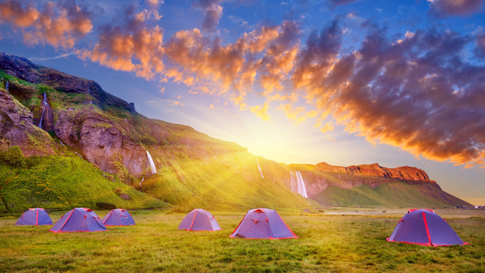 Tents dispersed in open field near Iceland waterfalls