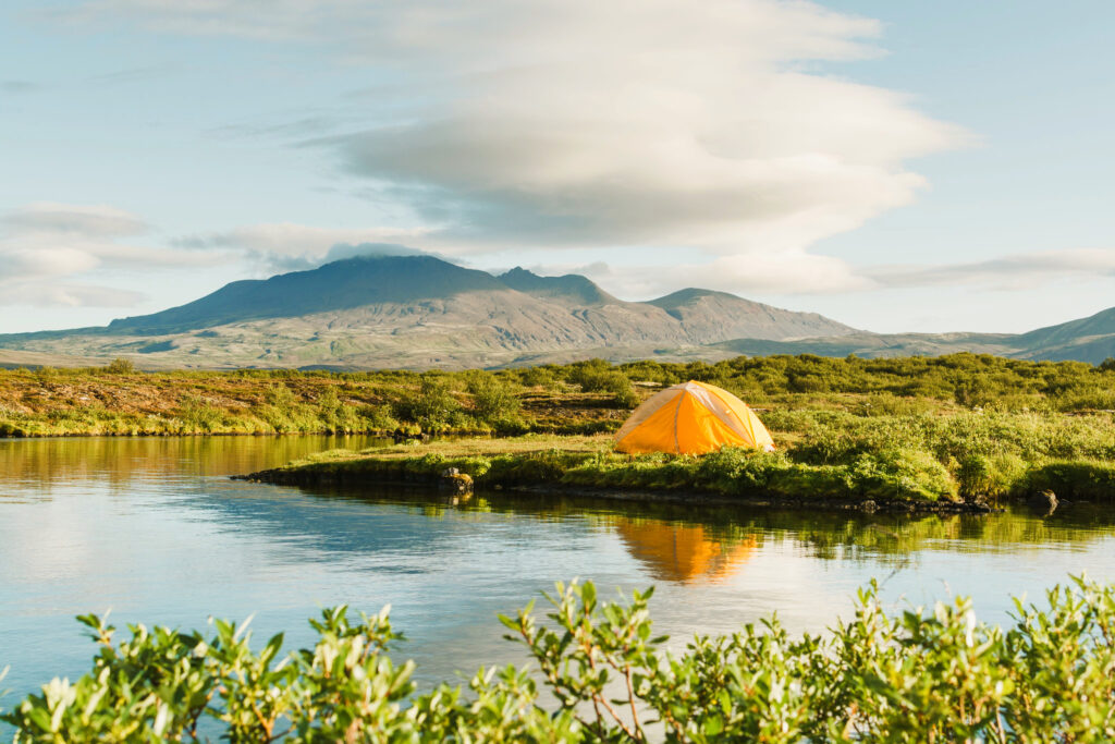 Tent sleeping by the water with large mountains in the background