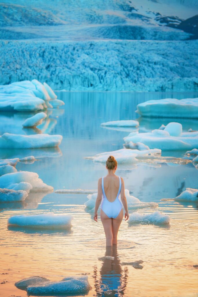 Girl in white swimsuit takes a dip in glacial waters in front of floating icebergs and a deep blue glacial wall of ice