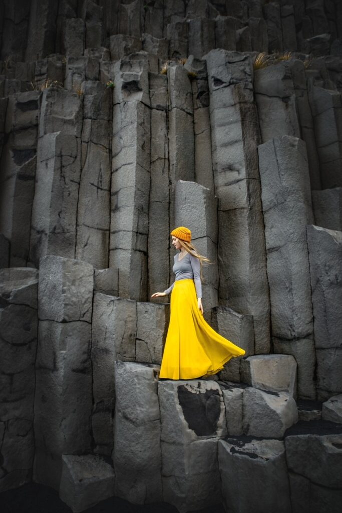 Girl in yellow skirt standing beside gray basalt columnar joints at an iceland instagram spot