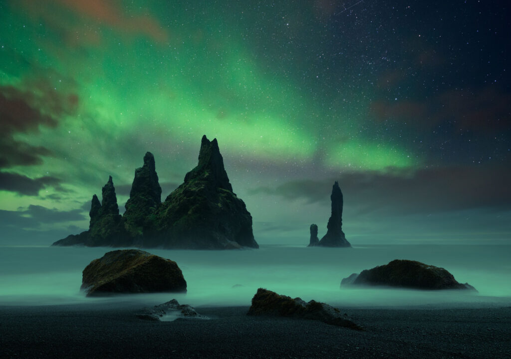 Sea stacks protruding from the soft flowing water and the northern lights surrounding them
