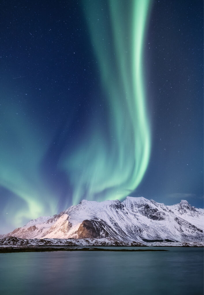 Snow covered mountains by the sea with green northern lights reaching up to the sky caught on camera with 