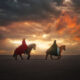 Guy and girl on horseback riding along the beach under a colorful sky