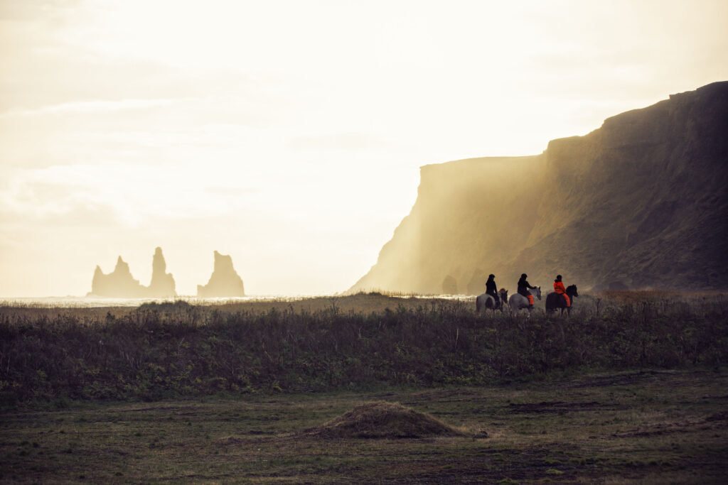 Moody scene of the horseback riding tours in Vik traveling along the Oceanside near towering sea stacks