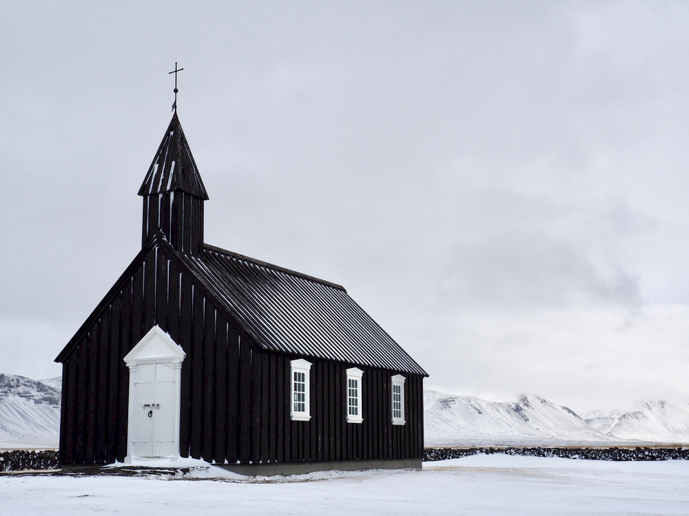 the Budir black church in the winter with the ground and mountains around it covered in snow