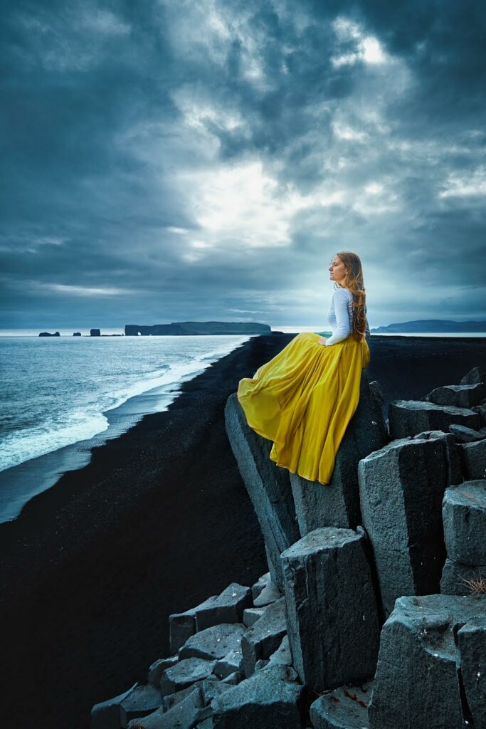 sitting on top of a basalt column at the Reynisfjara Black Sand Beach looking out at the Atlantic Ocean