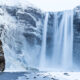 Skogafoss waterfall partially frozen in the wintertime with snow surrounding it