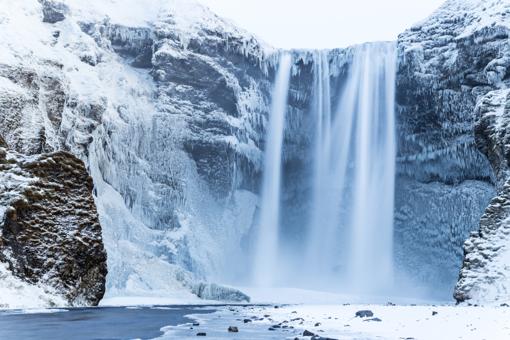 Skogafoss waterfall partially frozen in the wintertime with snow surrounding it