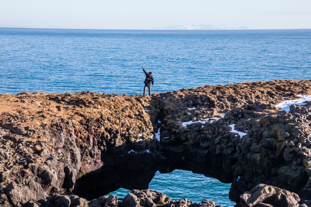 standing on top of the Arnarstapi natural bridge over the Atlantic Ocean with snow sprinkled over the rocks