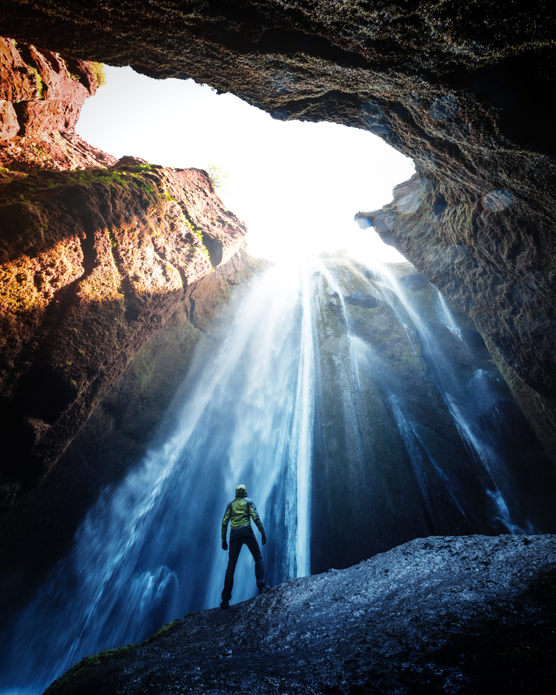 standing on a boulder at the base of the waterfall Gljufrabui watching the water stream through from the opening in the top of the cavern