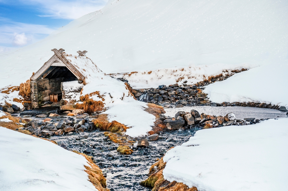 a snowy landscape and snow covered changing hut surround the Hrunalaug Hot Springs, a stop on your Iceland winter itinerary