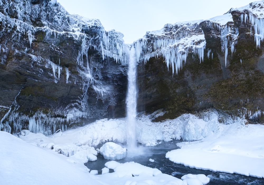 Kvernufoss waterfall slightly reduced in size due to being partially frozen with icicles and snow around it