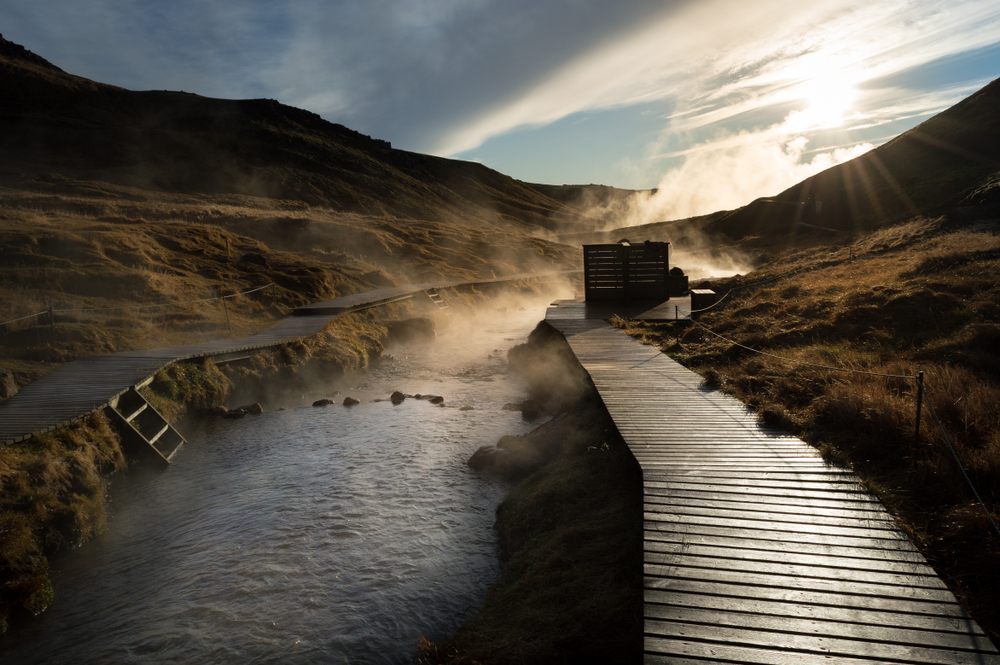 steam rising from the river water of the Reykjadalur Hot Springs on a sunny day as you complete your Iceland winter itinerary