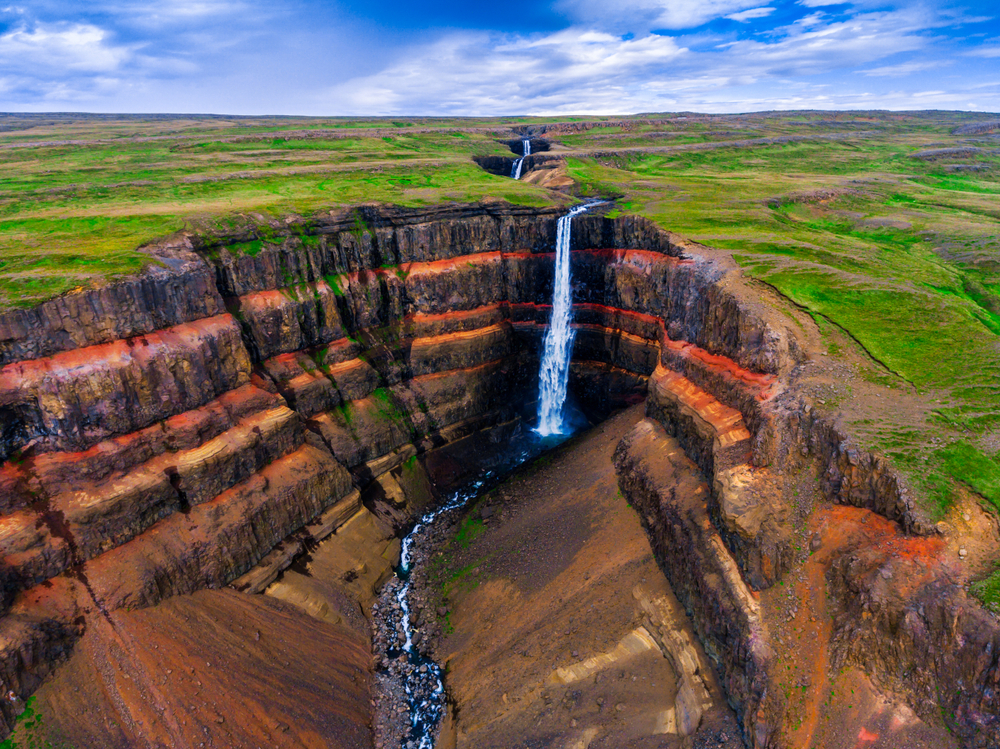  Aerial view of Hengifoss in a canyon with red and orange stripes.