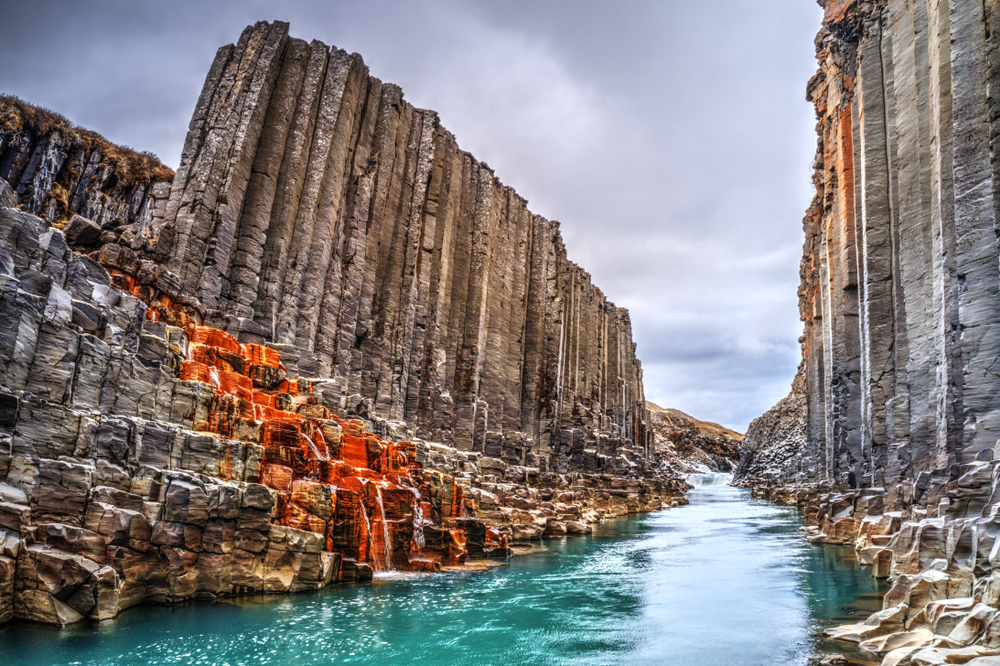 Looking through the Studlagil Canyon with basalt columns and blue water.