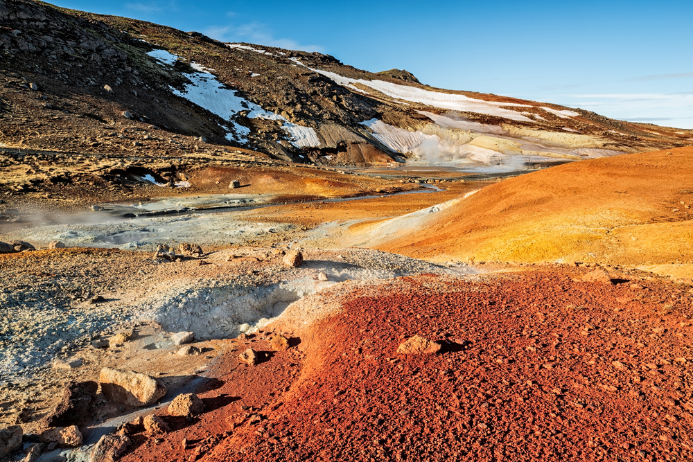 a sunny day at Krysuvik geothermal area where the landscape is covered in reds and yellows from the minerals and a little bit of snow