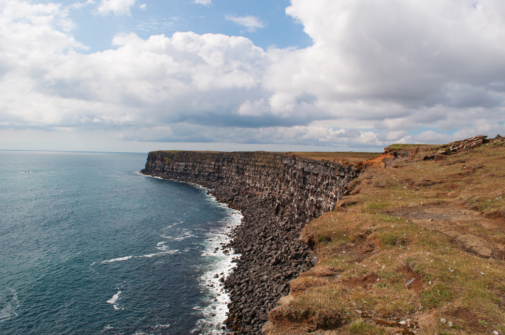 a view of the Krysuvikurberg Cliffs with the Atlantic Ocean to the left and a blue but cloudy sky above