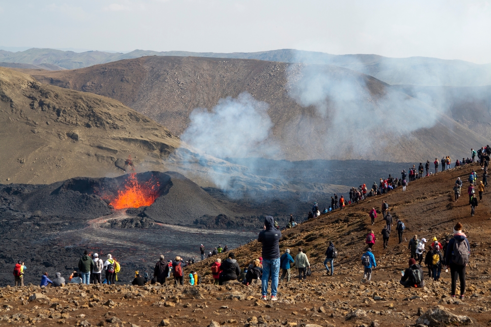 tourists and locals standing on the hillside watching the Meradalir volcano erupt and spew lava 