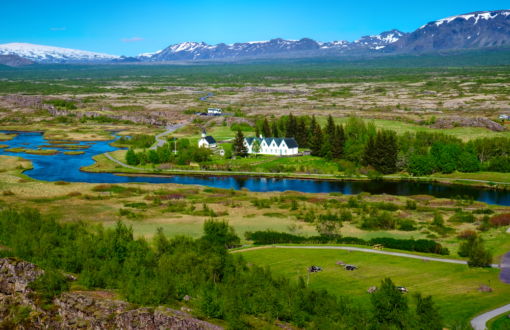 Landscape in the Thingvellir National Park in Iceland. The mountains are in the distance and you can see a church and some houses. The article is about where to stay on the Golden Circle 