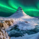Green northern lights over snow-capped Kirkjufell and Kirkjufellfoss waterfall in Iceland in February.