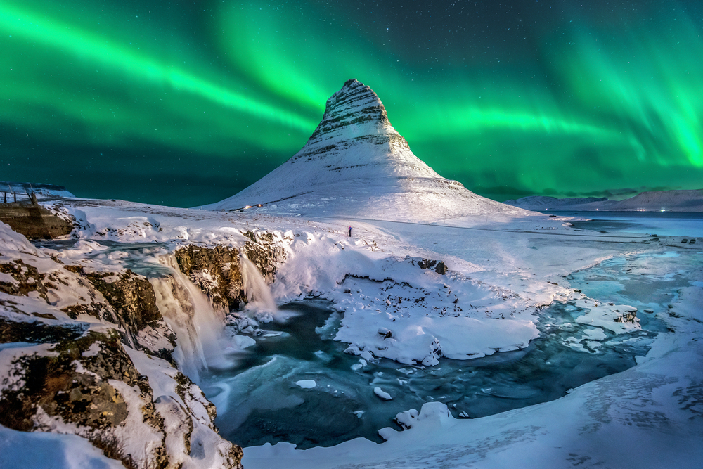 Green northern lights over Mount Kirkjufell and waterfall covered in snow.