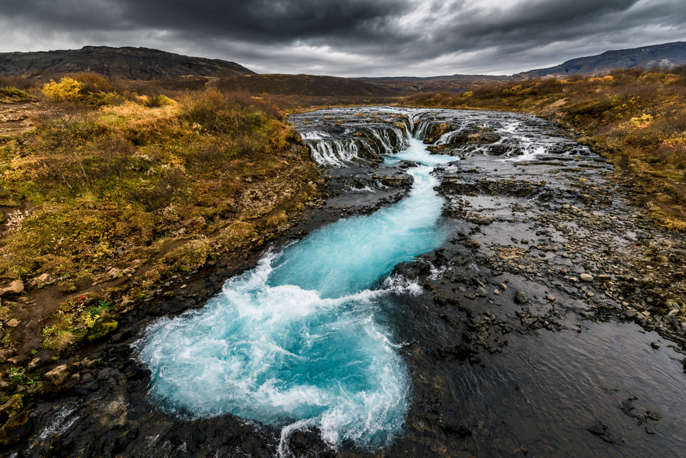 The bright blue Brúarfoss Waterfall on a cloudy day.