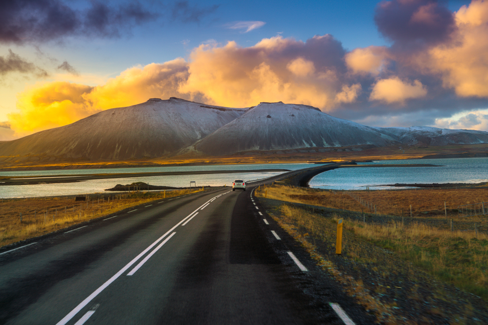 A white car driving down the Ring Road in Iceland at sunset.