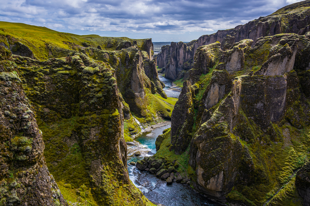 Rugged and mossy Fjaðrárgljúfur Canyon with a river running through it on a cloudy day during 3 days in Iceland.