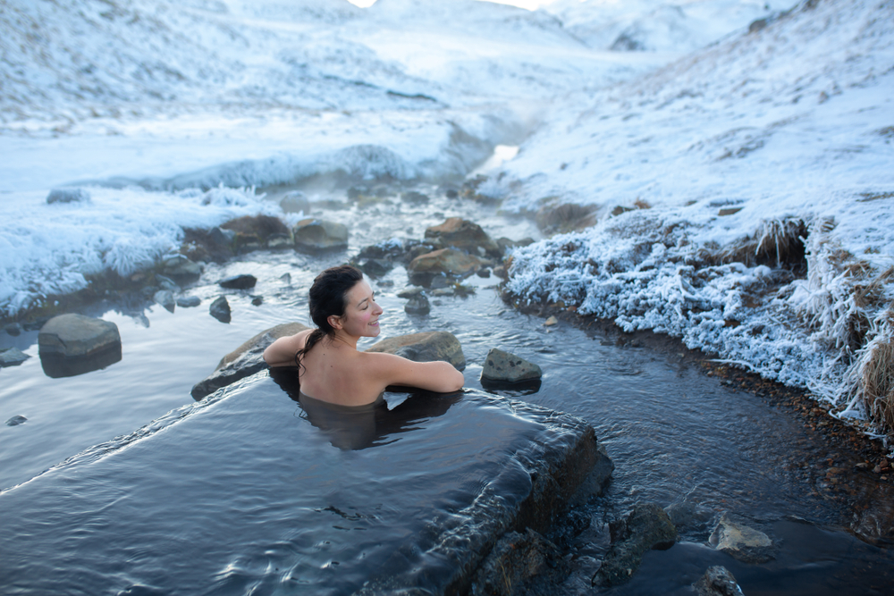 A person soaking in a natural hot spring in Iceland, surrounded by snow-covered rocks and the steamy warmth of the geothermal water in a winter landscape