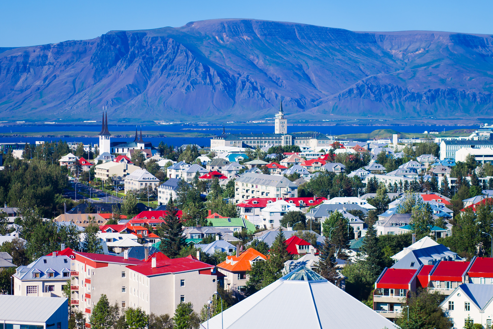 View overlooking the colorful rooftops of a Reykjavik neighborhood with the water and mountains in the distance.