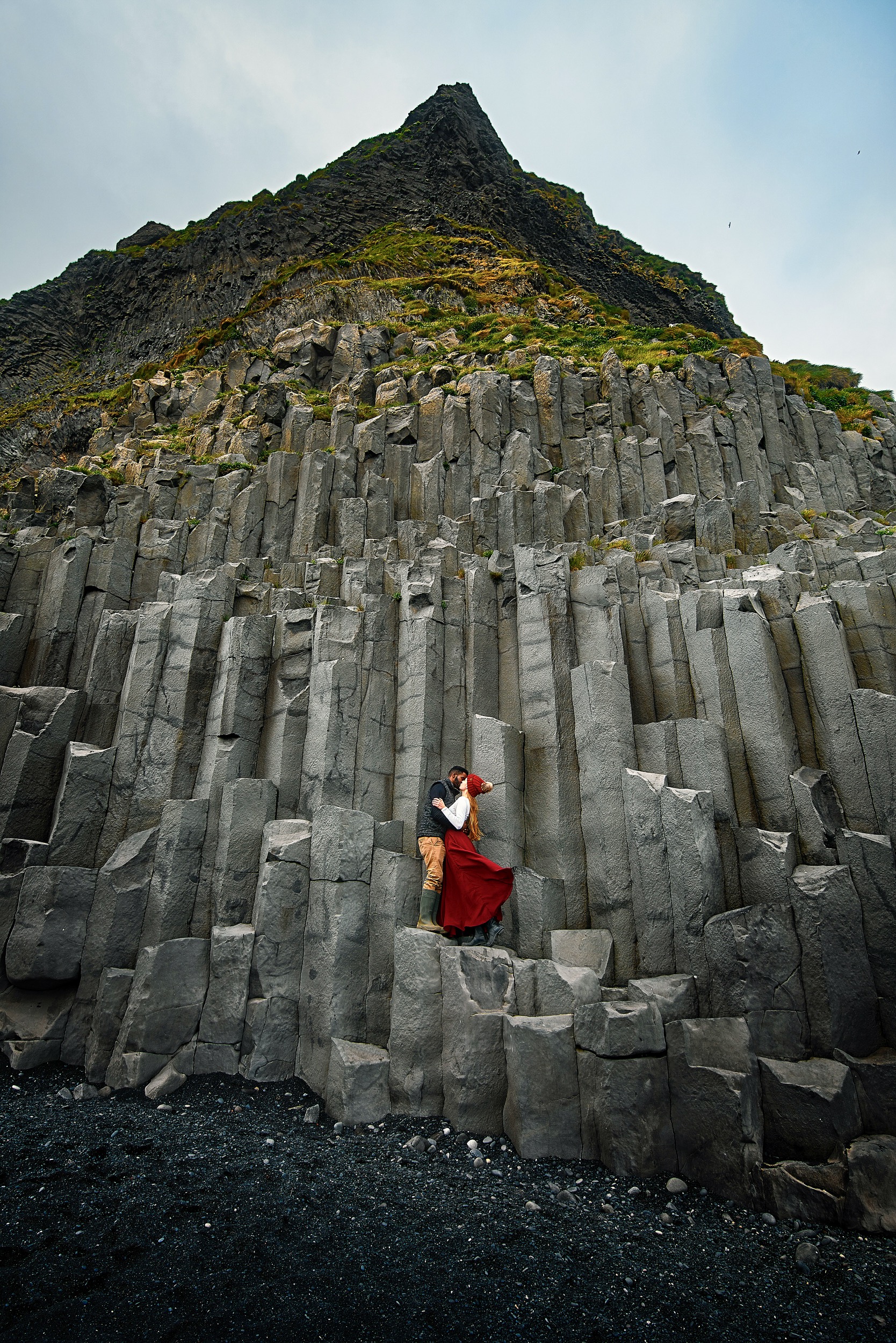 Couple kissing on black basalt columns over the black sand of Reynisfjara.