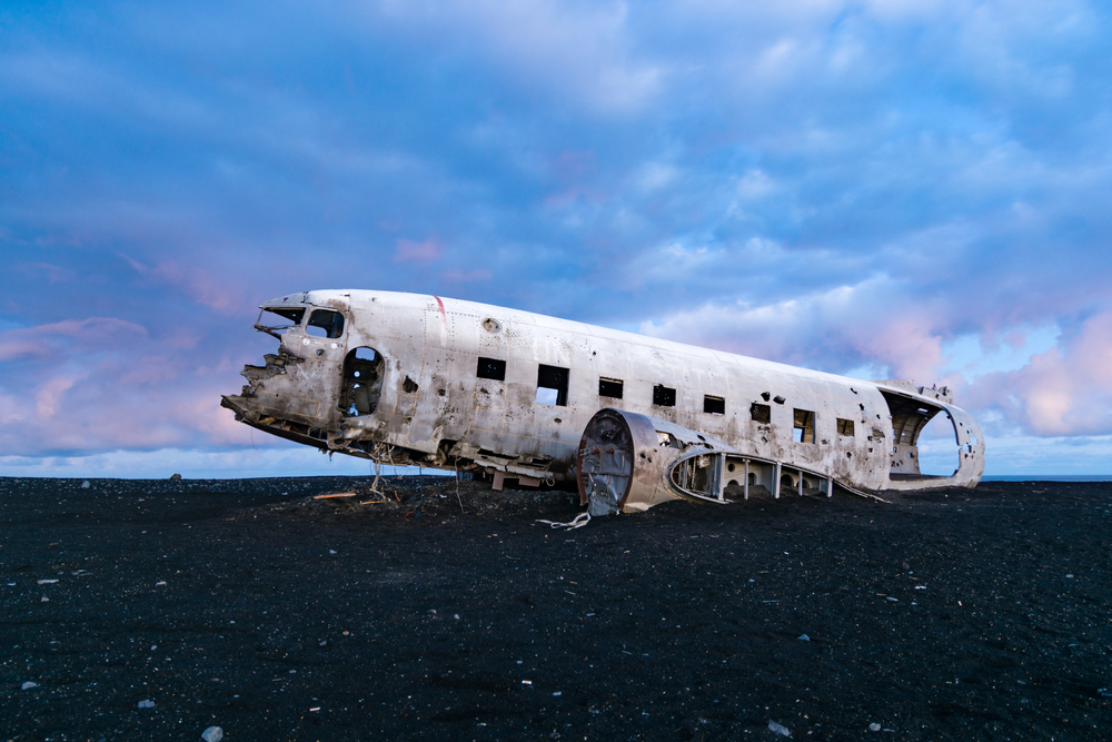 The Sólheimasandur plane wreak on a black sand beach under a sunset sky.