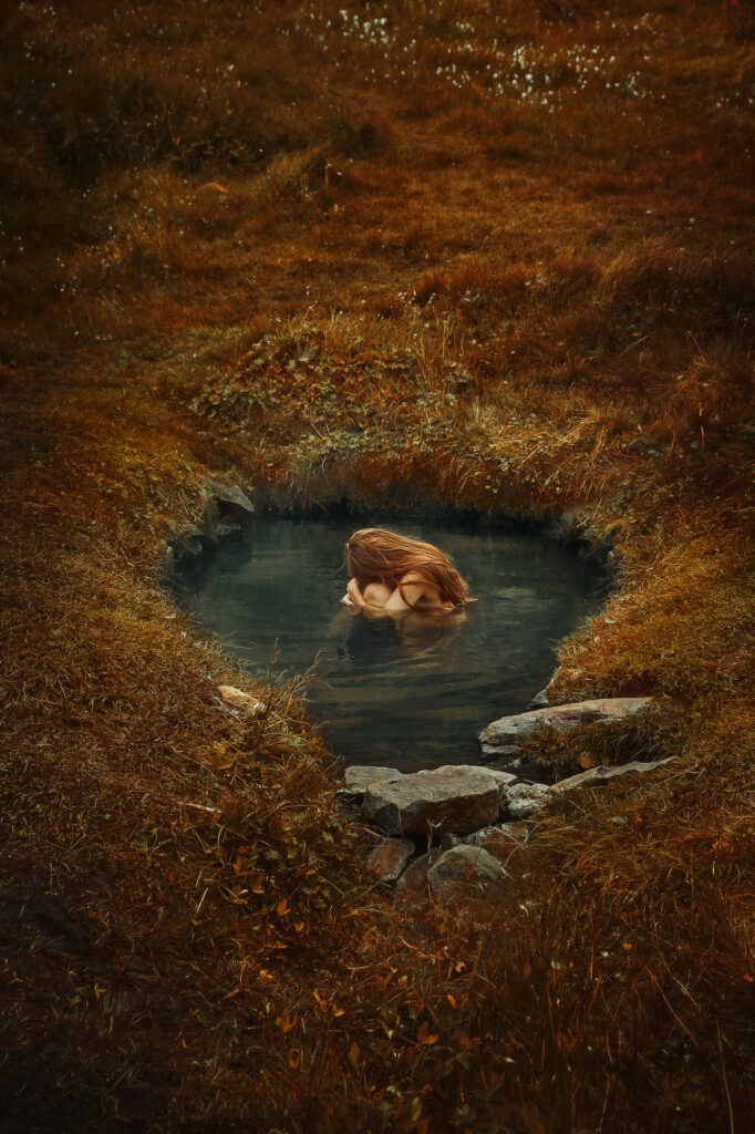 curled up in the water at of the Heydalur hot springs in the Westfjords that is a whole in the ground surrounded by grass