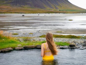 woman standing in a hot spring wearing a yellow bathing suit with a mountain in the background