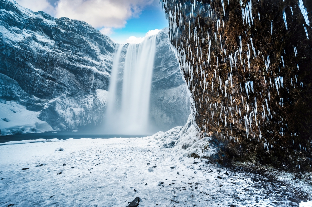 Skogafoss waterfall plummets into a snowy basin, surrounded by ice-clad cliffs, embodying the raw power and beauty of Iceland's winter