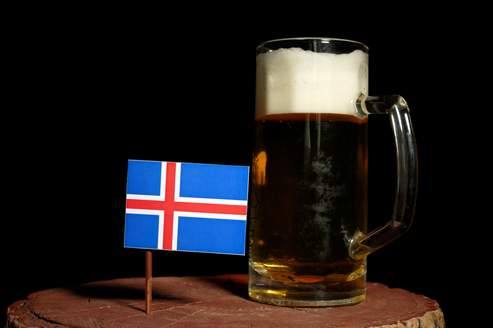 A cold mug of beer sits on a wooden stump, accompanied by an Icelandic flag, evoking a sense of national pride and local tradition.