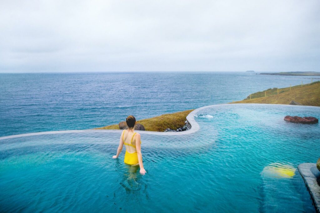 wearing a yellow bathing suit and looking out at the ocean from the wavy edge of the Geosea infinity pool