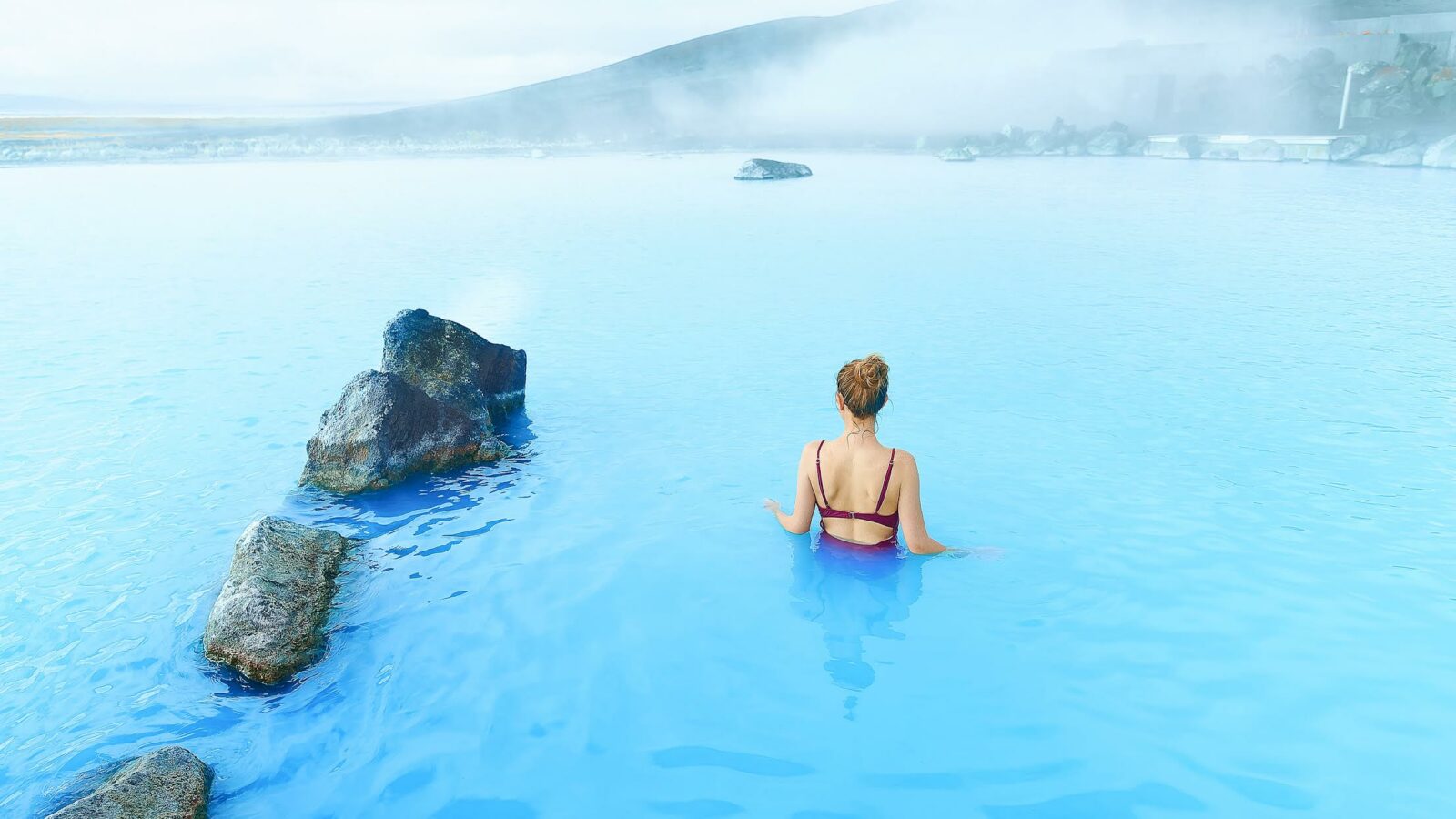 woman standing in myvtan nature baths blue water in iceland wearing a maroon swimsuit