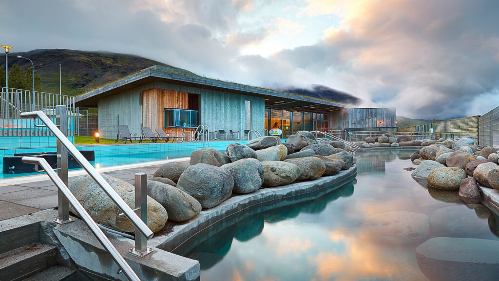 two levels of pools at Laugarvatn Fontana with rows of large rocks separating them with the main entrance building behind the upper pool