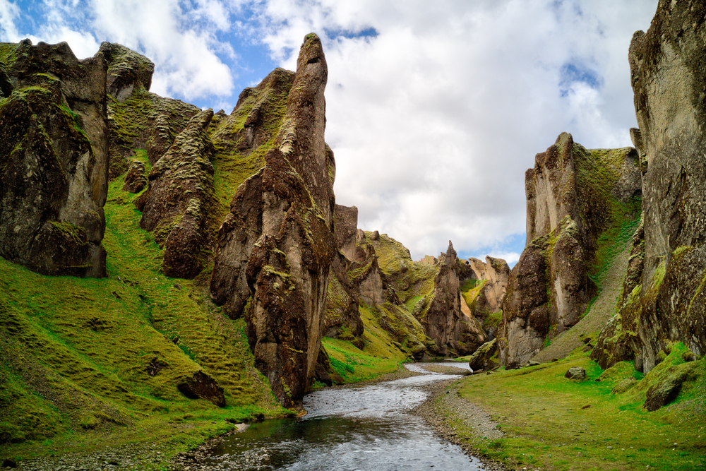 View from the bottom of Fjaðrárgljúfur Canyon with rugged, mossy walls and a stream in the bottom.