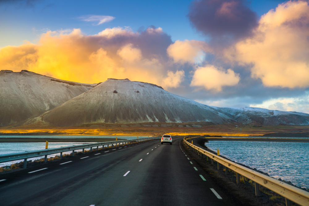 White car driving the Ring Road in Iceland at sunset with mountains and lakes.