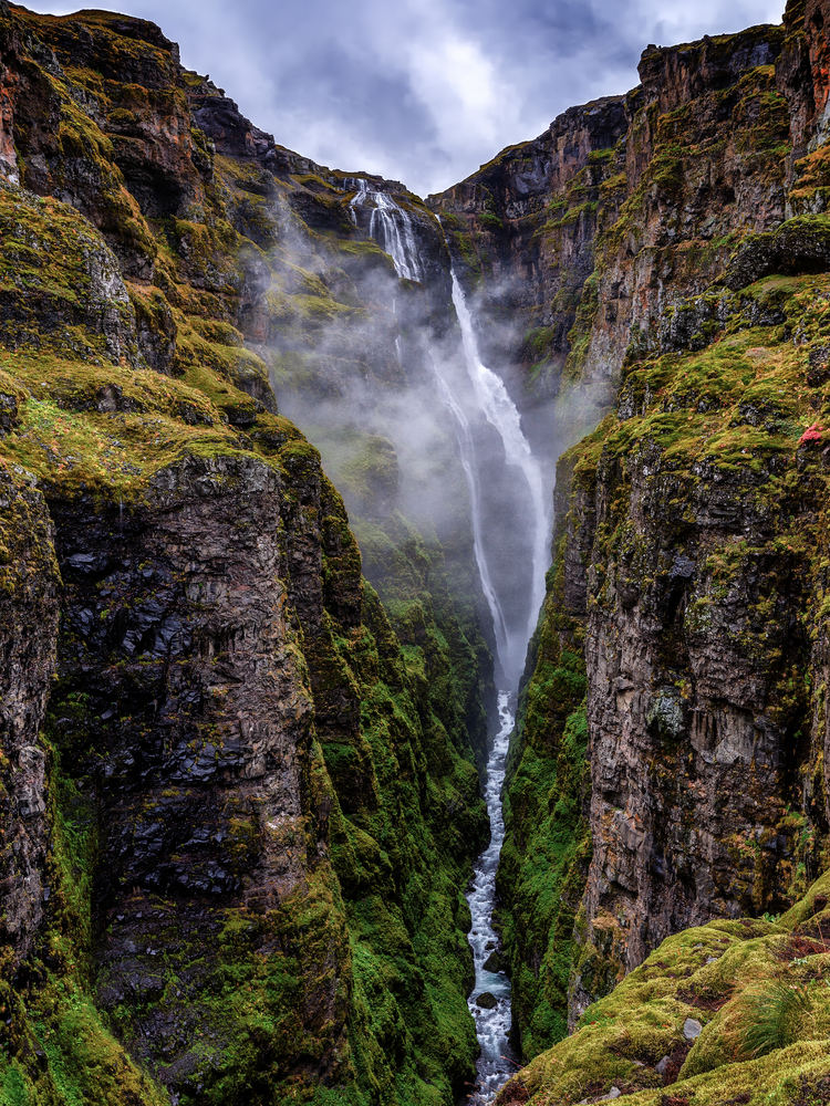 a view of Glymur Waterfall plunging down into a mossy canyon 