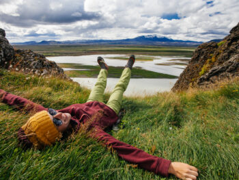 A woman lays in the greenery during her hike in Iceland, enjoying knowing what to wear in Iceland in may in her windbreaker, green pants and beanie.