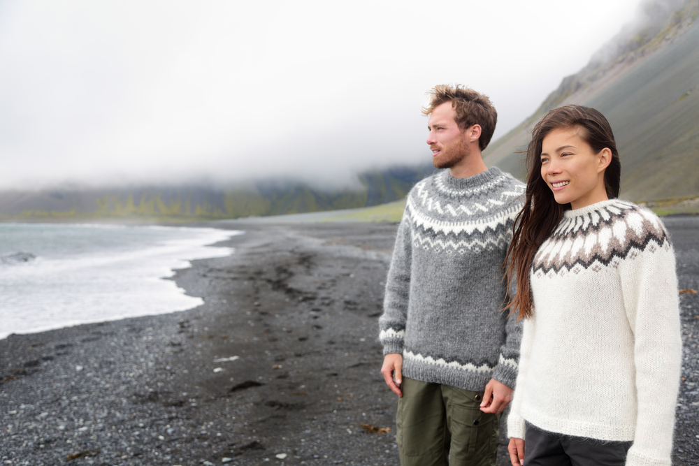 A couple knows what to wear to Iceland in August: they wear matching wool sweaters and cargo pants as they navigate the black sand beach.