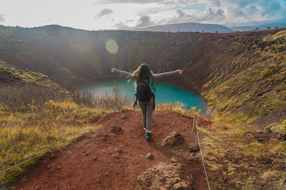 A tourist knows what to wear to Iceland in July on her hike: her hiking pants, long sleeve top and backpack prepare her for the views of the crater below.