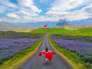 When wondering what to wear in Iceland in June, channel this model's freedom: her red jacket billows behind her as she runs in her thermal layers down a street with purple flowers on either side of her, tower da church in the distance.