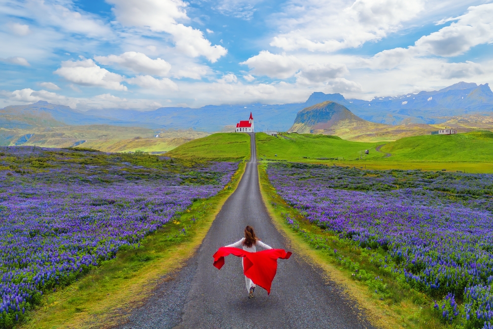 When wondering what to wear in Iceland in June, channel this model's freedom: her red jacket billows behind her as she runs in her thermal layers down a street with purple flowers on either side of her, tower da church in the distance.