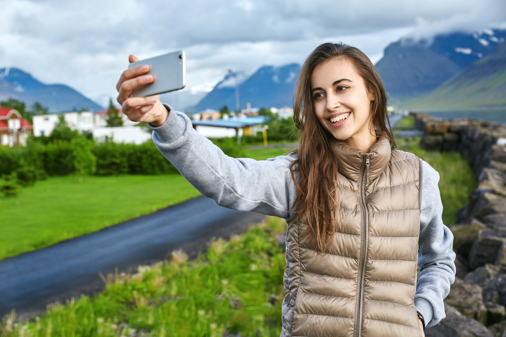 A woman takes a selfie in Iceland, not wondering what to wear in Iceland in June, as she I comfortable with her sweatshirt and puffer jacket. 