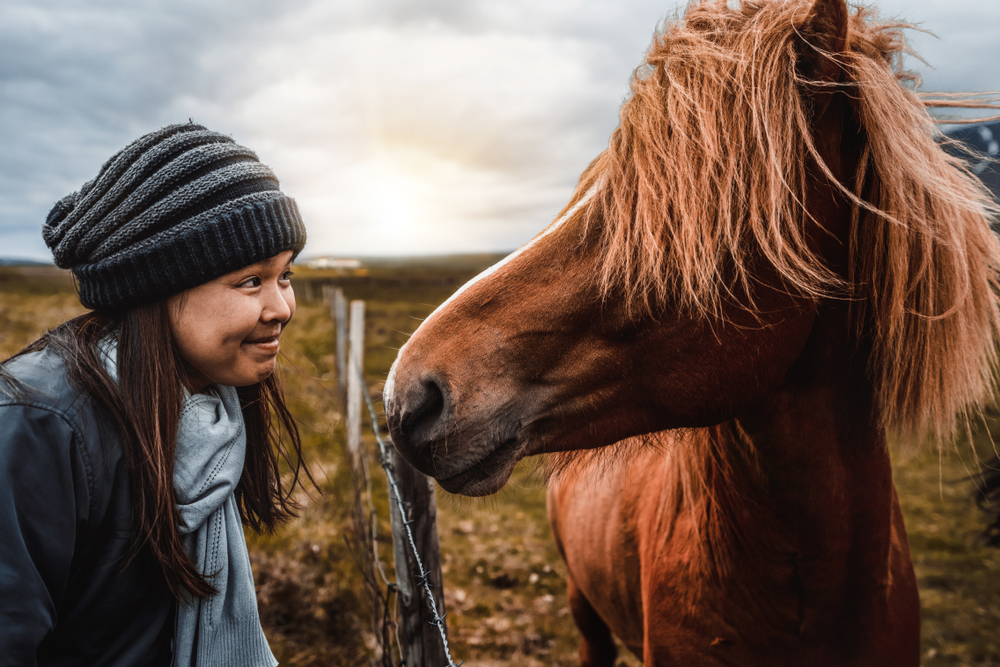 A young girl smiles at a horse in Iceland while wearing her beanie and scarf: she was prepped because she knew things people forget when packing for iceland.